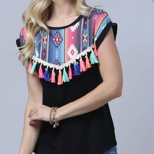 Mujer usando blusa negra con estampado tribal multicolor en el pecho y flecos decorativos de colores, estilo boho moderno.