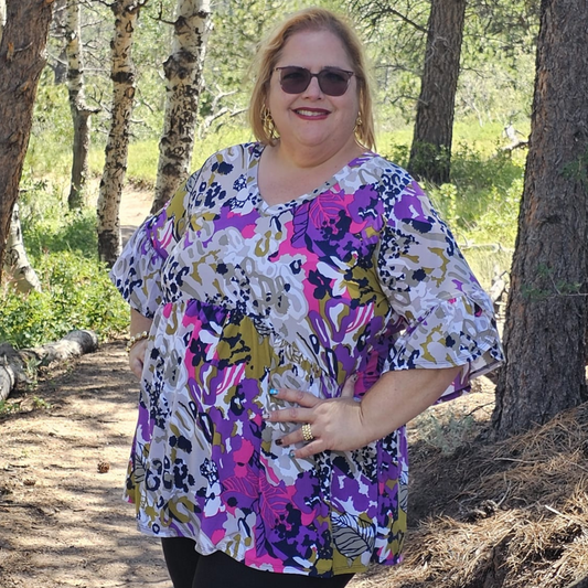 Blusa de mujer con estampado floral abstracto en tonos fucsia, púrpura, blanco y mostaza, mangas tres cuartos con vuelo y corte amplio tipo túnica.