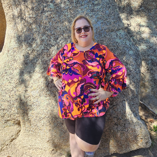 Blusa de diseño psicodélico en tonos naranja, fucsia y púrpura con mangas largas acampanadas y estampado llamativo, ideal para un look colorido y moderno.