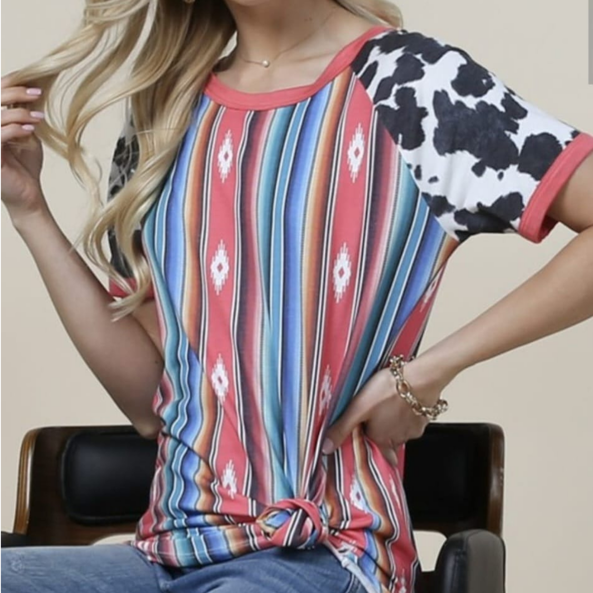 Mujer usando blusa casual con estampado tribal multicolor y mangas con print de vaca, con nudo decorativo en la parte baja del frente.