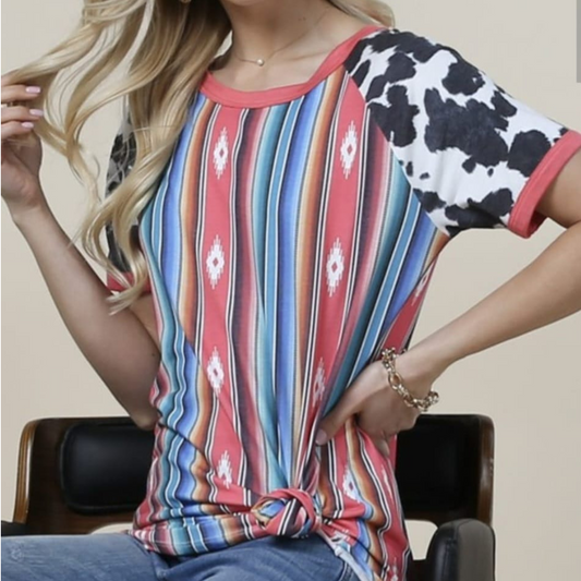 Mujer usando blusa casual con estampado tribal multicolor y mangas con print de vaca, con nudo decorativo en la parte baja del frente.