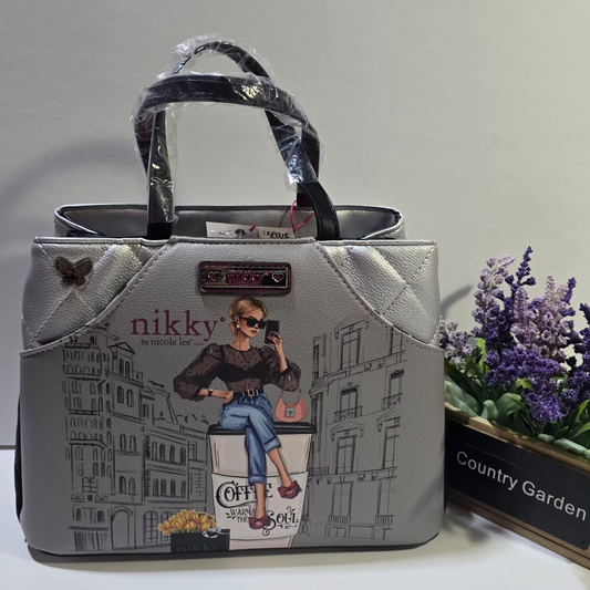 Cartera Nikky by Nicole Lee color gris con ilustración de mujer fashionista, asas negras y detalles decorativos.

