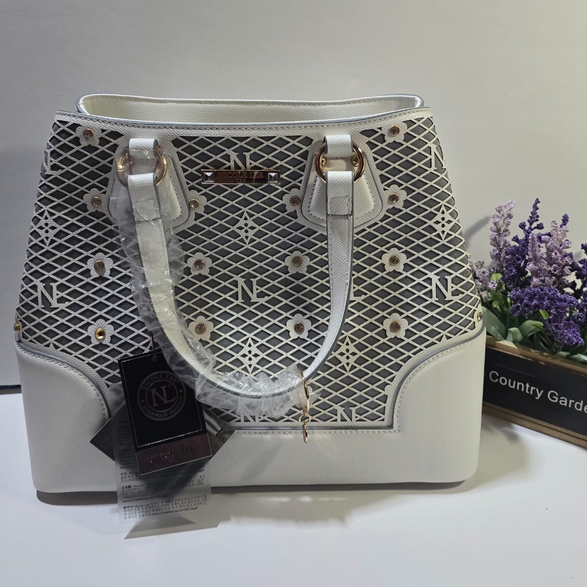 Cartera tote blanca de cuero sintético con diseño de malla gris y detalles florales, asas dobles y herrajes dorados.