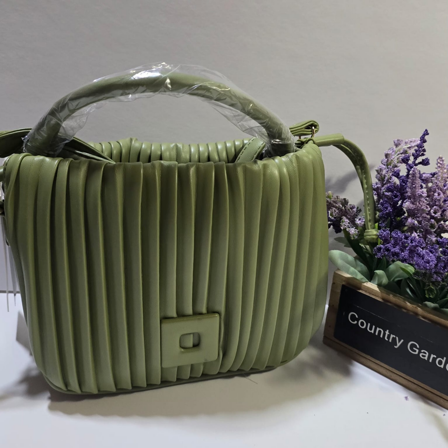 Cartera verde oliva con textura plisada, asa superior acolchada y correa ajustable estilo moderno y versátil.

