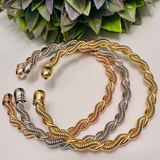 Tres pulseras trenzadas de acero inoxidable en colores oro, plata y oro rosa, con diseño espiral y acabado brillante, sobre fondo claro.