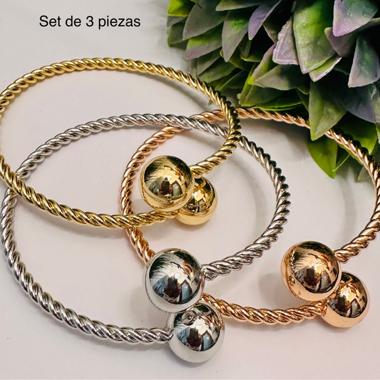 Set de tres pulseras rígidas de acero inoxidable en colores oro, plata y oro rosa, con diseño trenzado y esferas metálicas brillantes en los extremos, sobre fondo blanco.