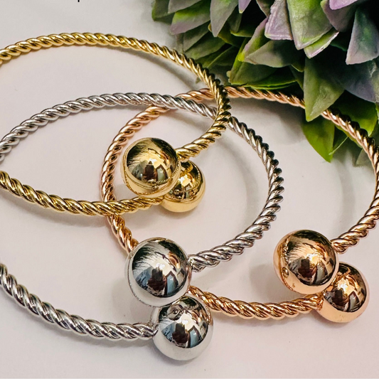 Set de tres pulseras metálicas torcidas con esferas brillantes en colores dorado, plateado y oro rosado.