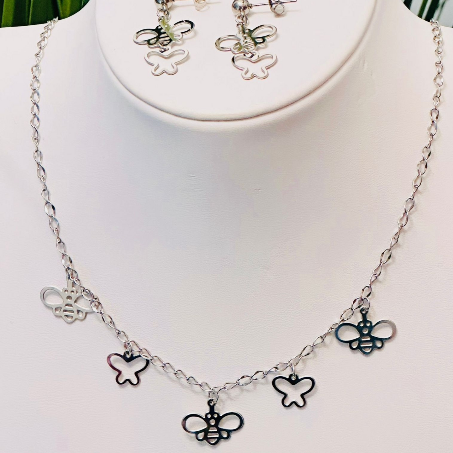 Set de collar y aretes en acero inoxidable con dijes huecos en forma de mariposas y abejas.