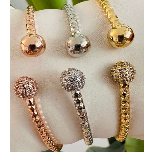 Set de tres pulseras rígidas en tonos dorado, plateado y oro rosa con textura facetada y esferas lisas o decoradas con cristales, presentadas sobre un cojín blanco.